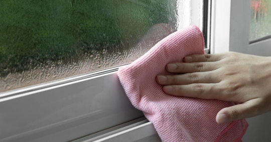 Woman's hand wiping condensate from window glass