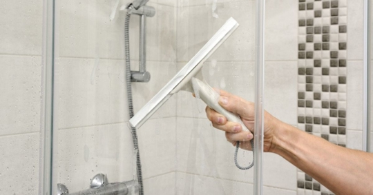 Person cleaning shower glass with rubber squeegee